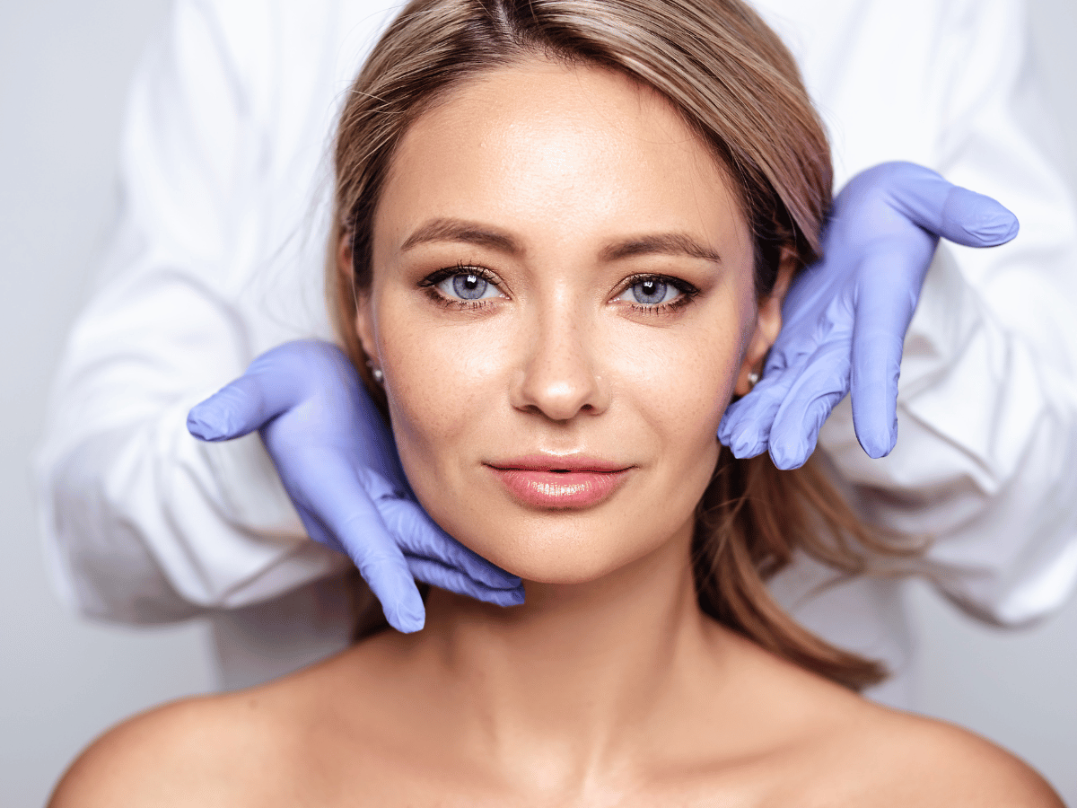 A woman at the dermatologist looking at the camera while the providers hands are examining her face.