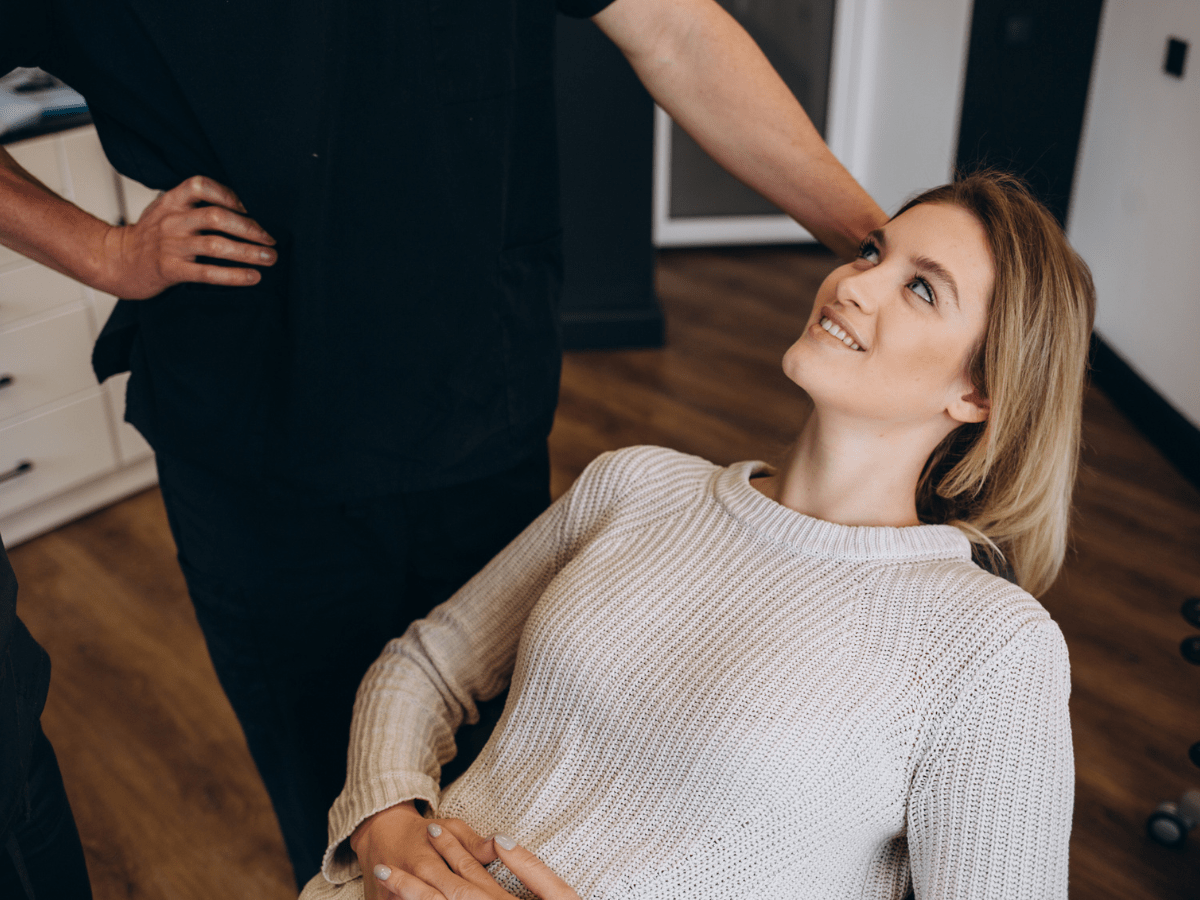 A woman talking to a dermatologist in her office while laying in the consultation chair and smiling.